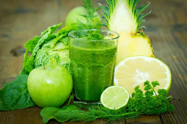 A green smoothie is surrounded by other fruits and vegetables.
