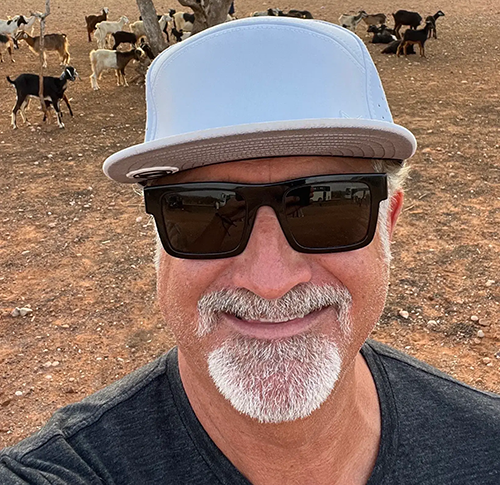 A man with sunglasses and a hat in front of some deer.