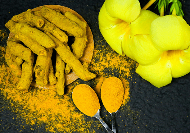 A bowl of turmeric next to spoons and flowers.