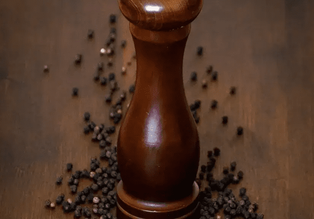 A pepper mill sitting on top of some black peppercorns.
